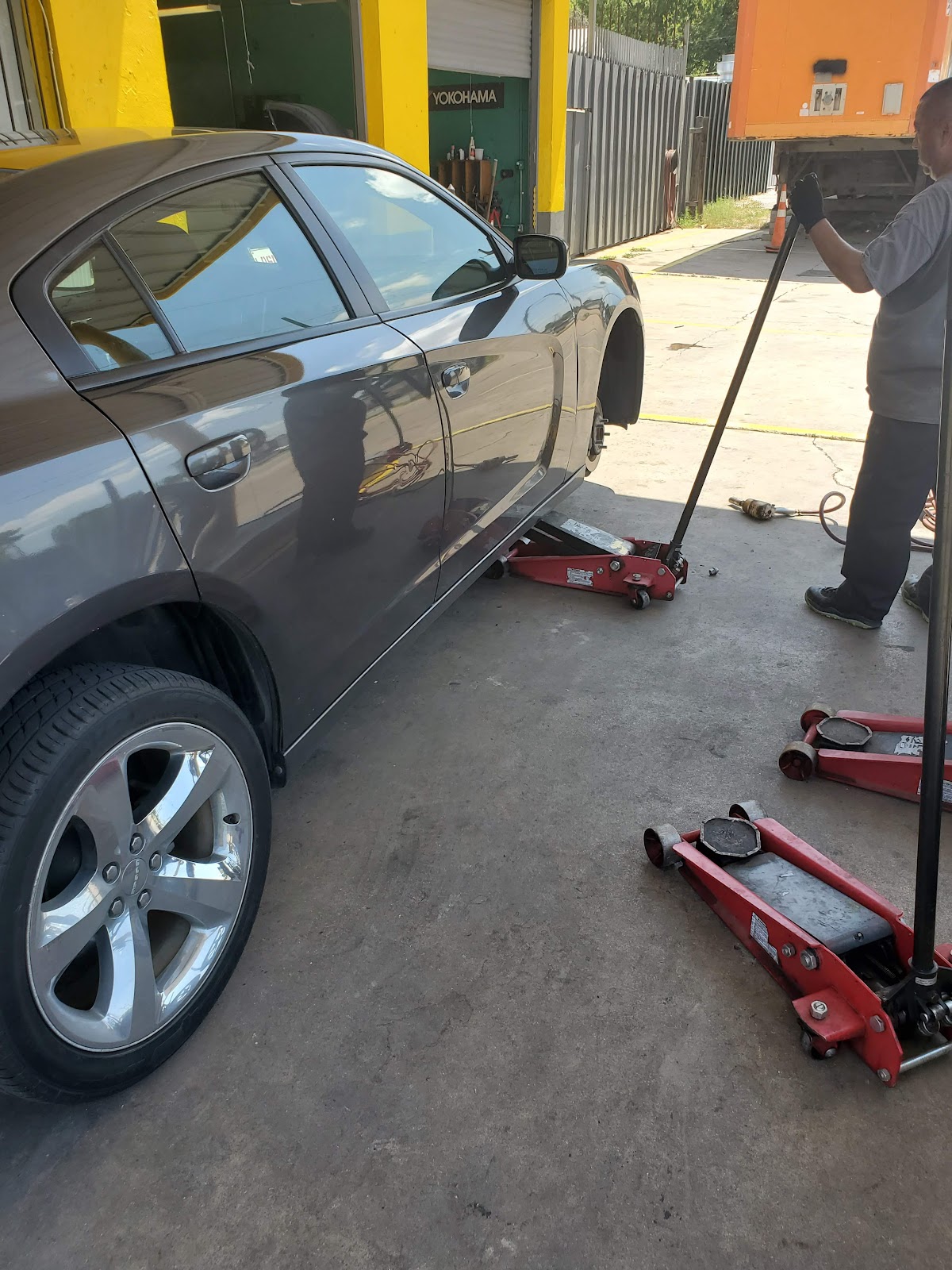 A technician at Leal's Tire Shop lifting a car on a jack next to the Yokohama tire display