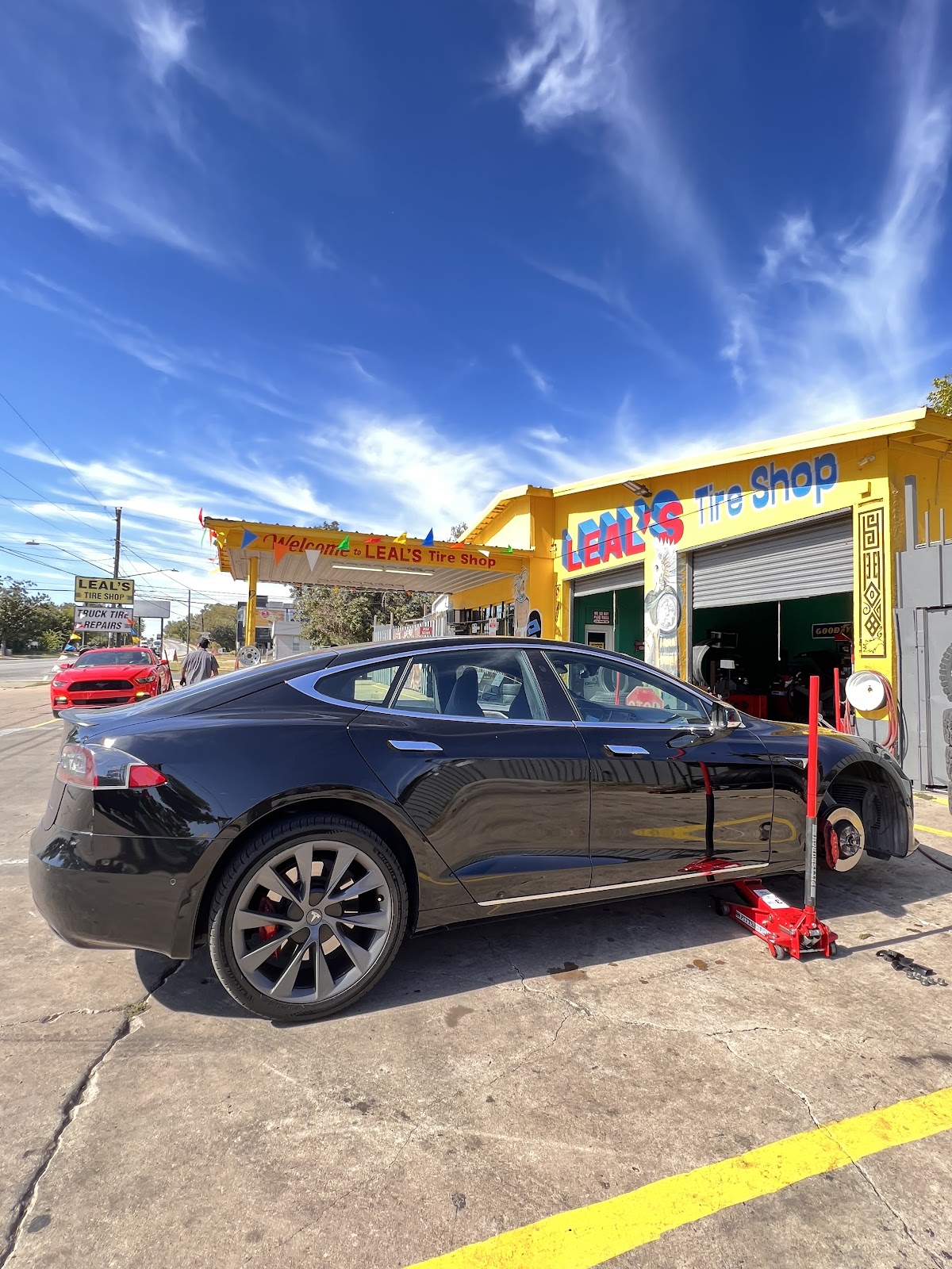 A Tesla being serviced outside Leal's Tire Shop under the Welcome to Leal's Tire Shop banner